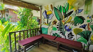 Una habitación con un banco de madera, un mural de plantas tropicales y un techo de bambú.