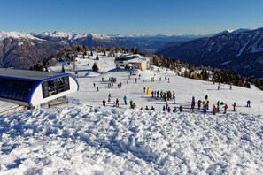 A ski resort with a chairlift, a building with a sloped roof, and a snowy landscape with mountains in the background.
