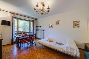 Una habitación con una cama, una mesa de comedor con sillas, una araña y una ventana con cortinas.