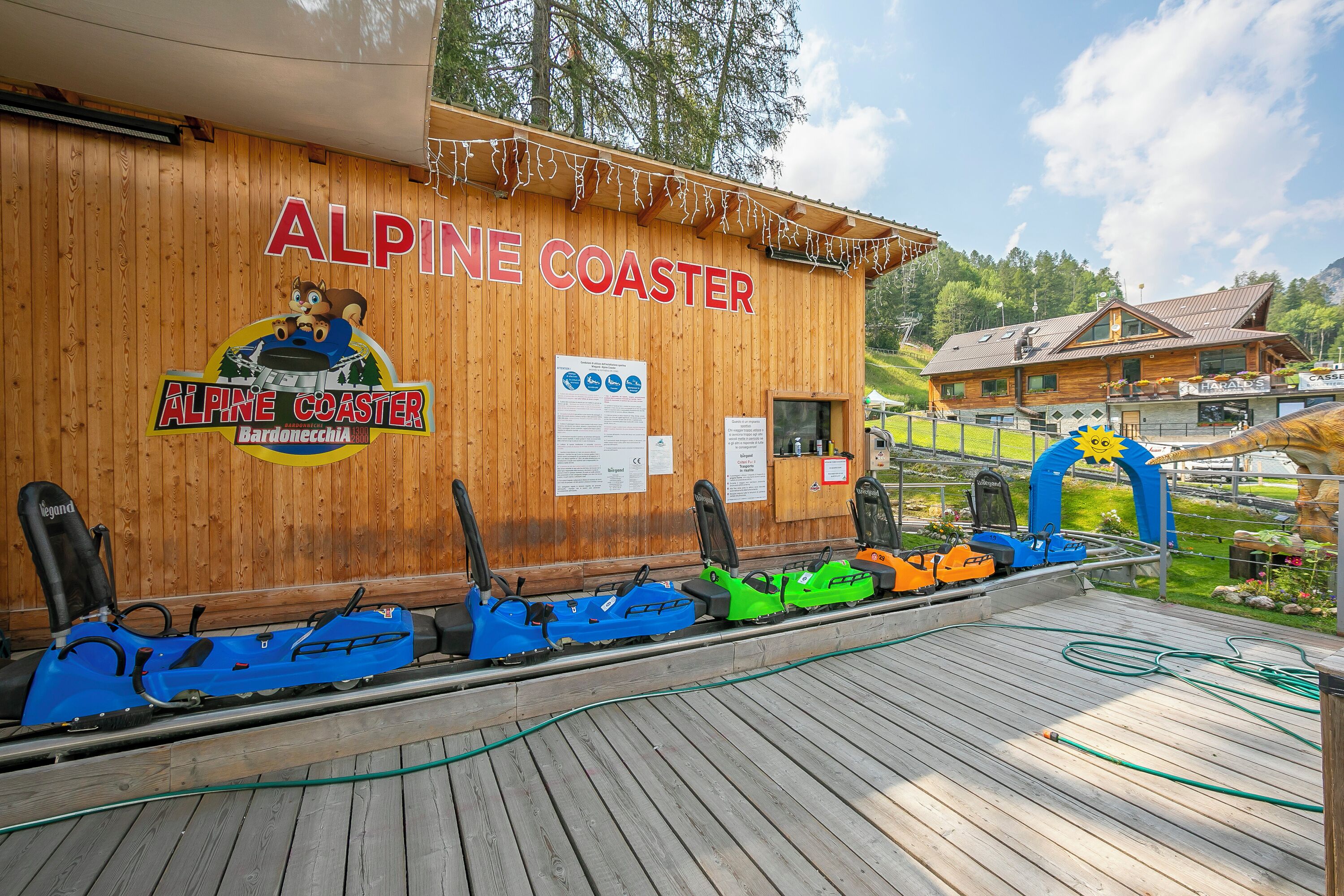 A wooden Alpine Coaster building with a sign, a logo, and a row of snowmobiles.