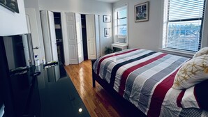 Un dormitorio con cama, armario, escritorio y ventana con persianas.
