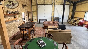 A spacious indoor area with a high ceiling, a central table with chairs, a sofa, and a fireplace. - The Woolybugger Barn (Cameron)
