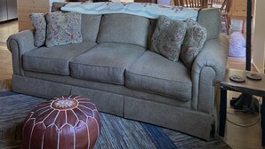 A cozy cabin interior with a sofa, ottoman, and dining area. - The Woolybugger Barn (Cameron)