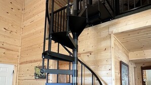 A spiral staircase in a wooden cabin with a loft bedroom above. - The Woolybugger Barn (Cameron)
