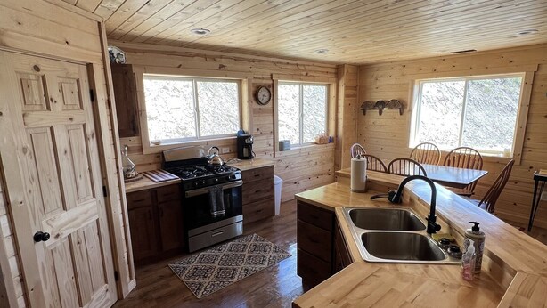 A wooden cabin interior with a kitchen featuring a stove, sink, and wooden cabinets. - The Woolybugger Barn (Cameron)