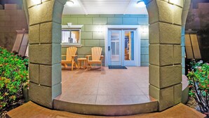 Un arco de piedra que da acceso a una habitación con una puerta, una mesita y dos sillas.