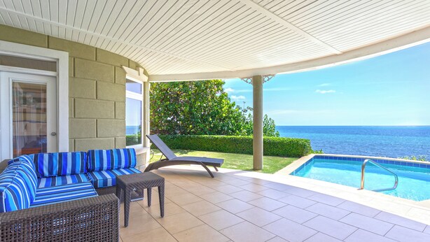 Un espacio al aire libre techado con una piscina, un sofá y una silla de relax.