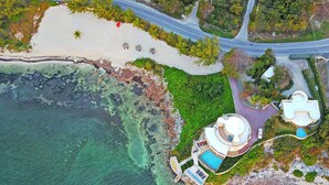 Vista aérea de una propiedad costera con piscina, playa y camino.