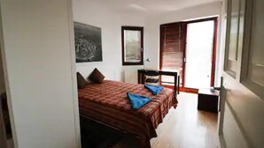 Un dormitorio con cama, una silla, un escritorio y una ventana.