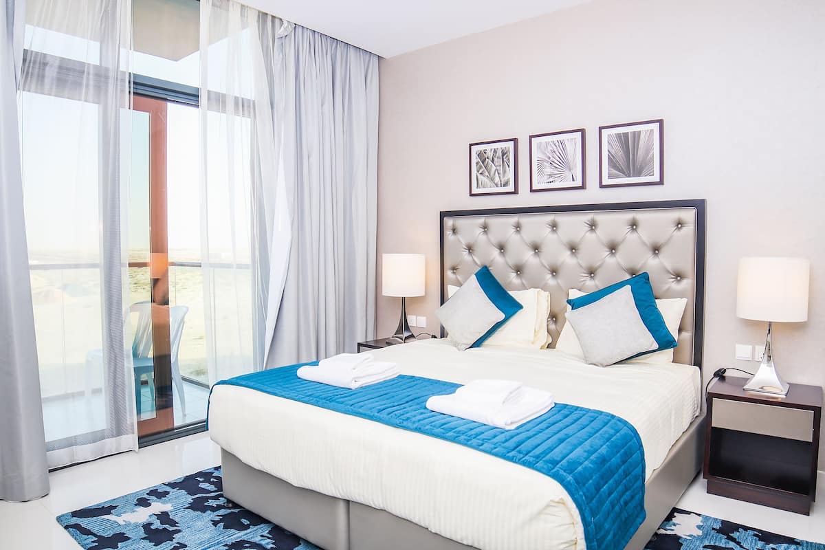 Quarto de hotel com uma cama grande, duas mesas de cabeceira, uma janela com cortinas e três quadros na parede.