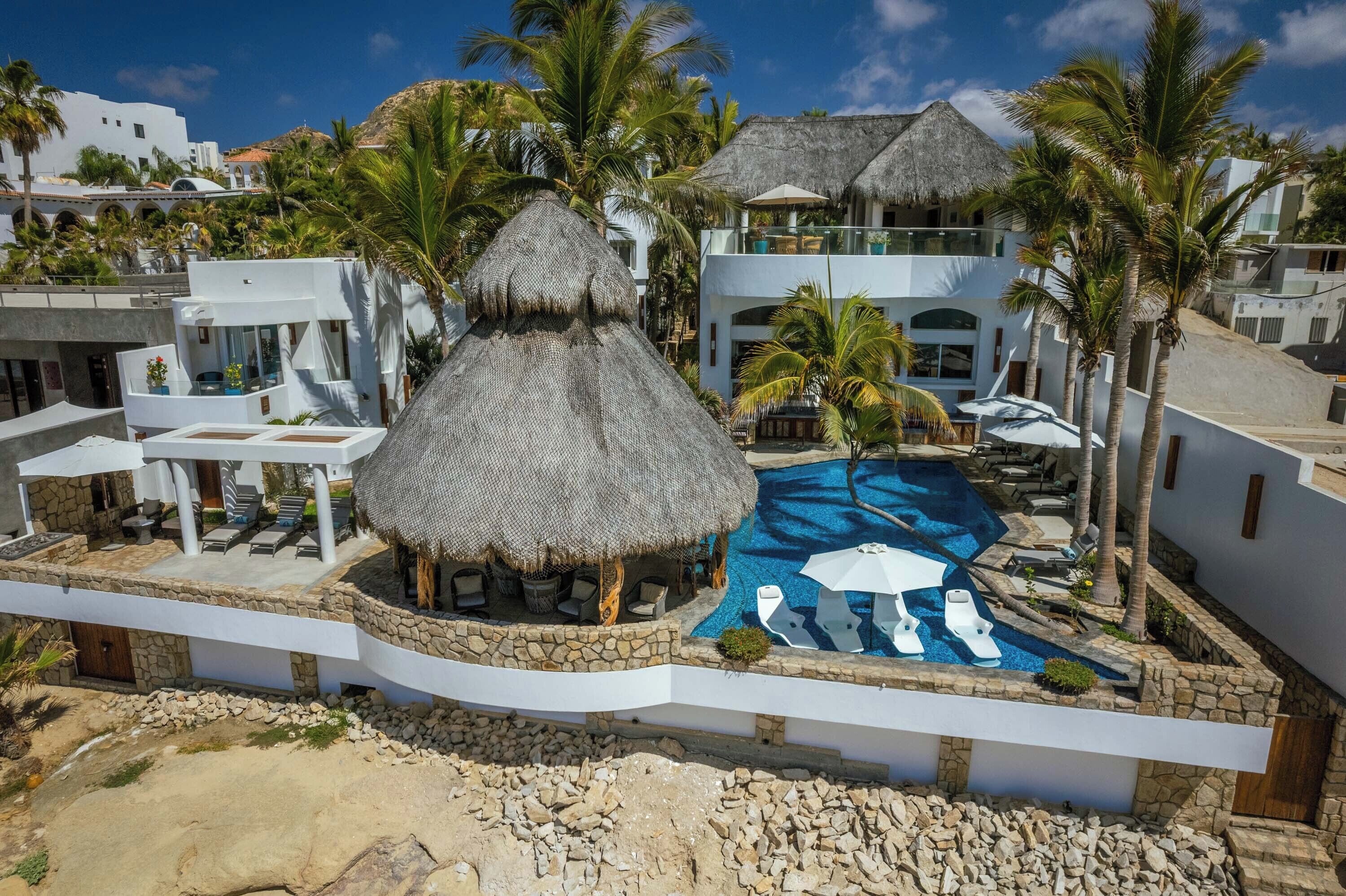 A resort with a swimming pool, thatched-roof structures, and palm trees.