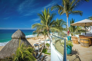 A beachside hotel with a thatched-roof structure, lounge chairs, and a glass balustrade overlooking the ocean.