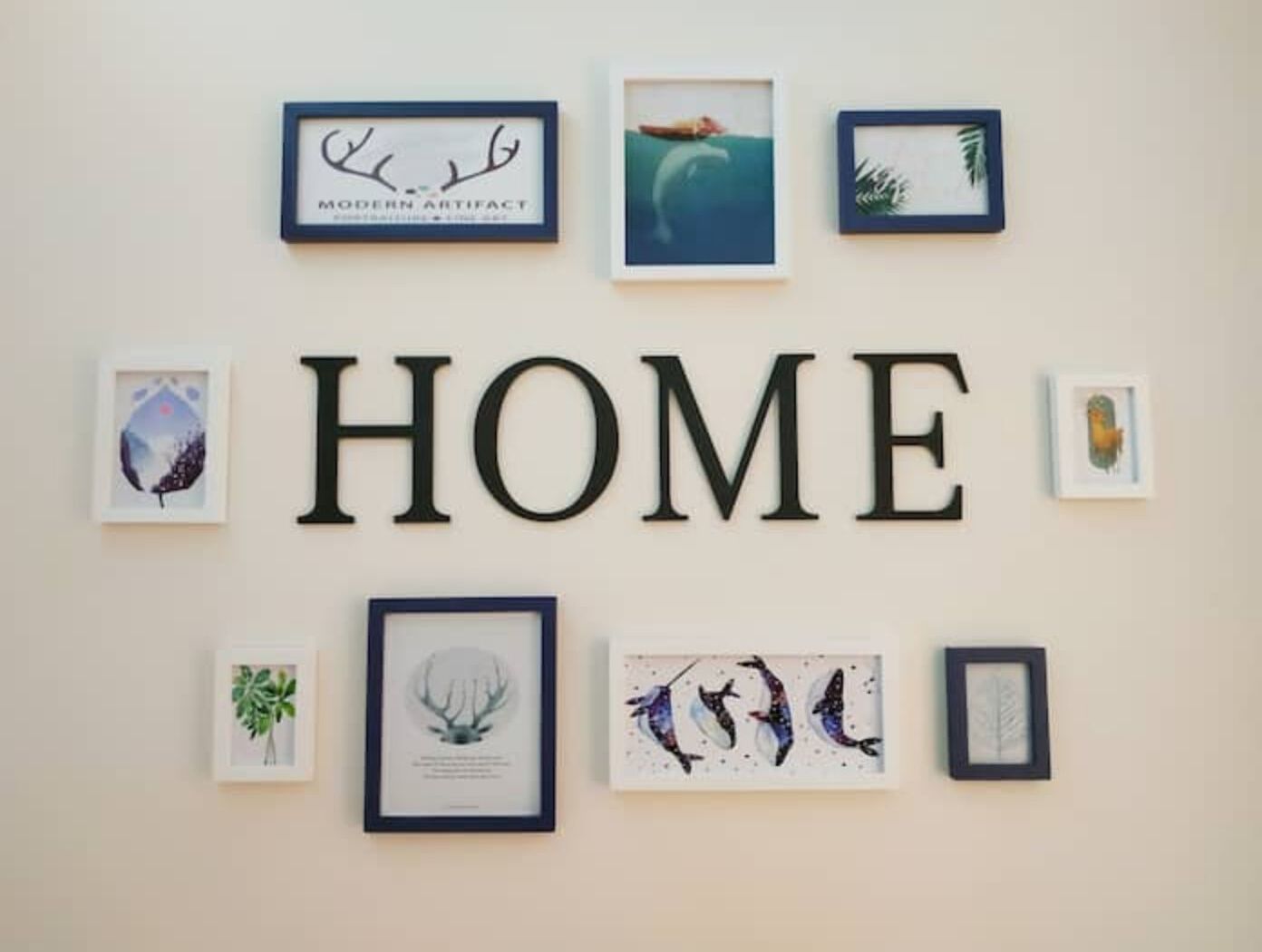 Eine Wand mit gerahmten Kunstwerken und dem Wort „HOME“ in großen Buchstaben.