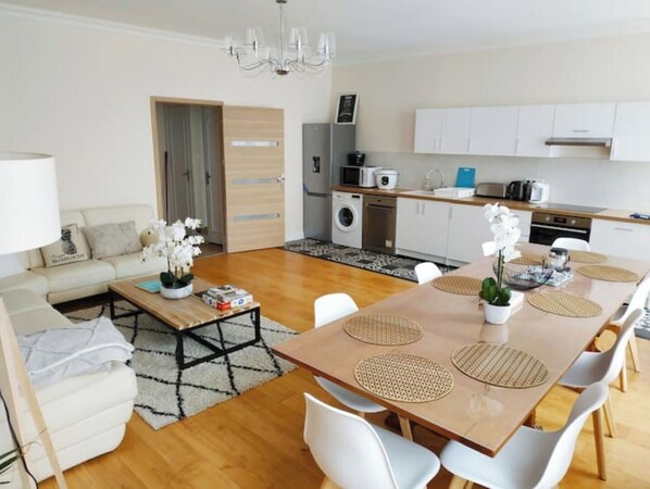 Un salon moderne avec une table à manger en bois, des chaises blanches, un canapé et une table basse.