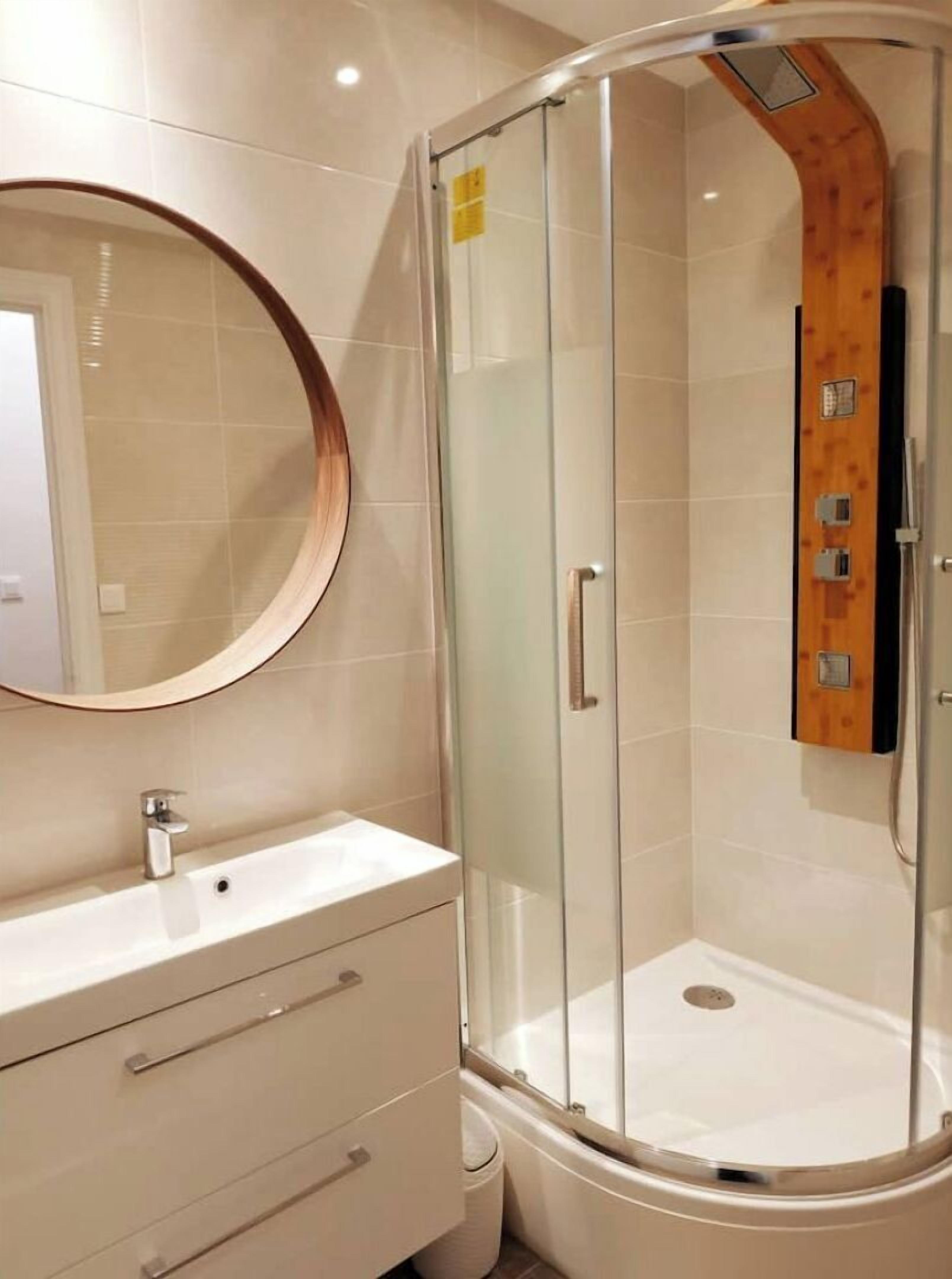 A modern bathroom with a glass-enclosed shower, a round mirror, and a white vanity with drawers.