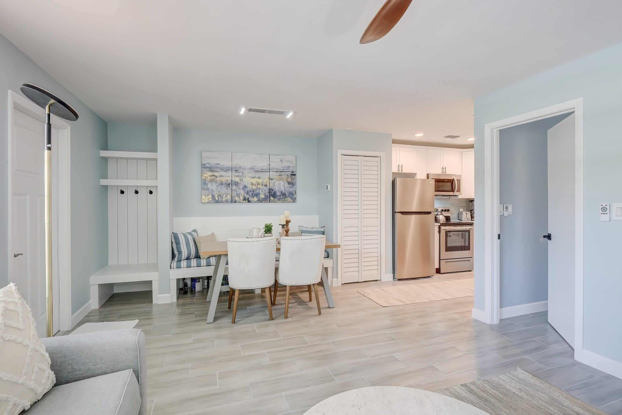 A modern kitchen with stainless steel appliances, a dining area with a white table and chairs, and a living space with a sofa and a coffee table.
