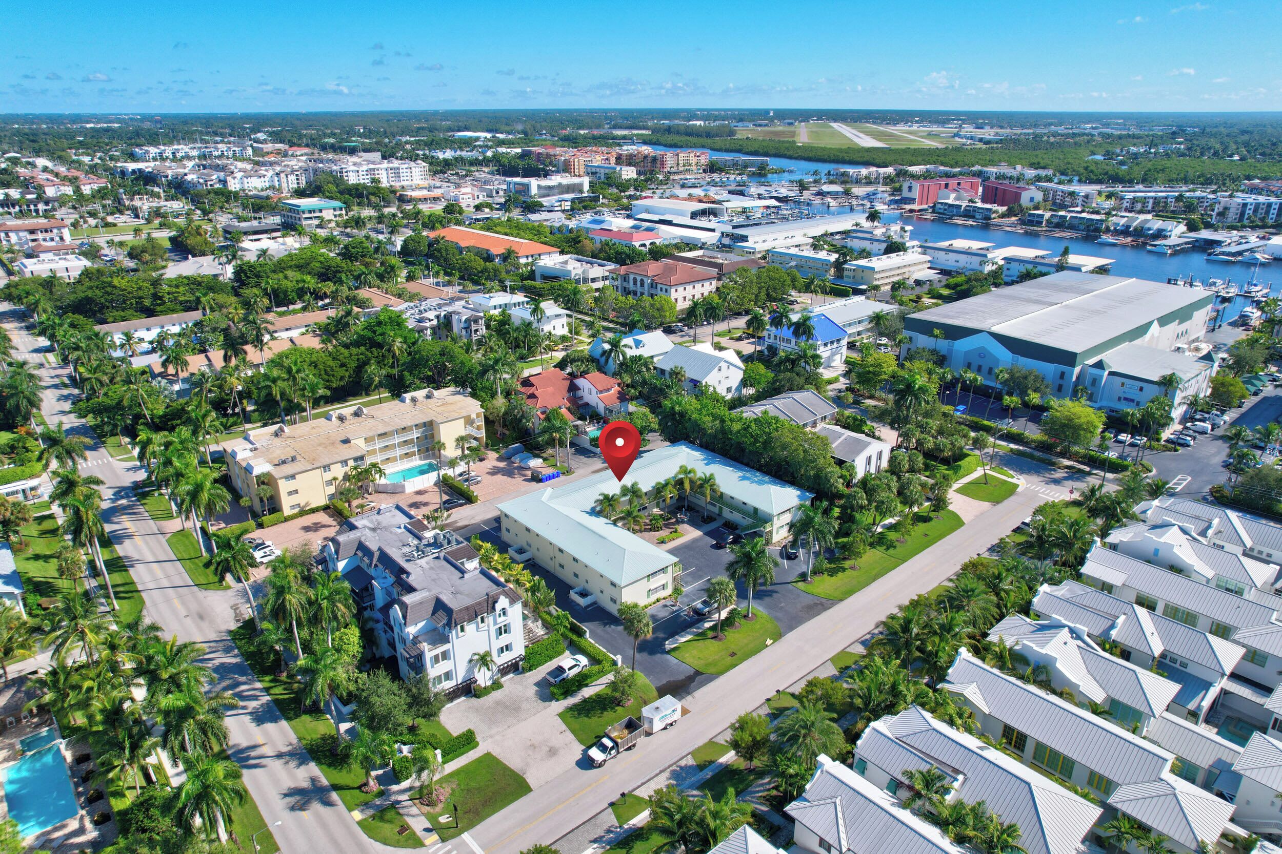 An aerial view of a coastal town with a marina, residential buildings, and a prominent hotel with a blue roof.