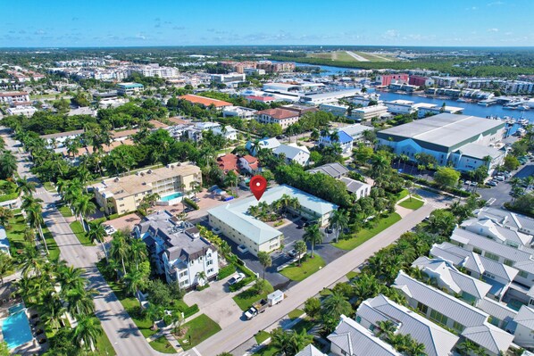 An aerial view of a coastal town with a marina, residential buildings, and a prominent hotel with a blue roof.