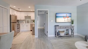Een moderne keuken met witte kasten, een roestvrijstalen koelkast en een eethoek met een grijze console tafel.