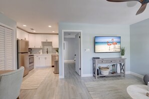 A modern kitchen with white cabinets, a stainless steel refrigerator, and a dining area with a gray console table. - Walk to the Beach and Downtown Naples From Our Totally Upgraded Condo (Naples)