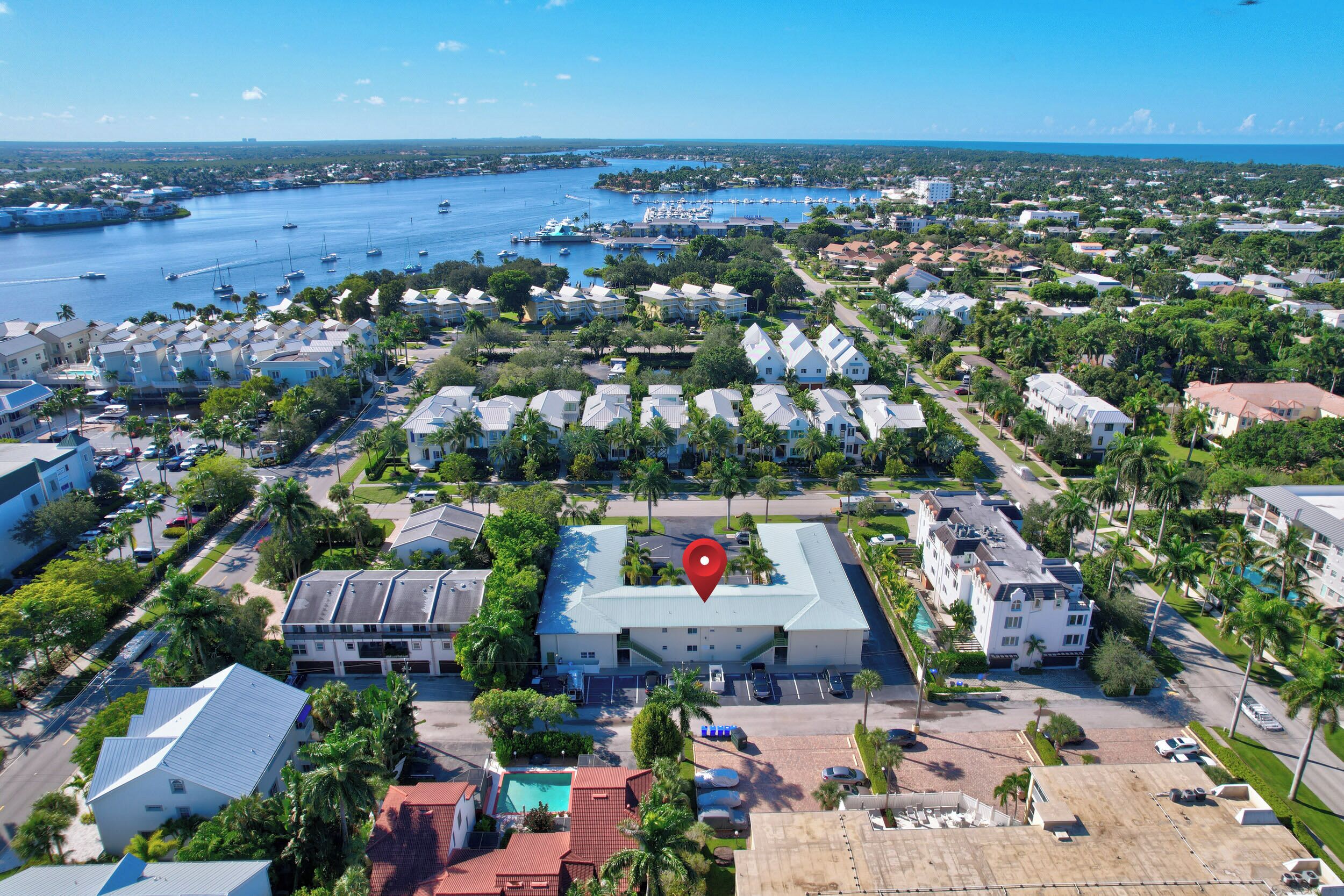 A coastal residential area with a marina, houses with varying roof styles, and a central building marked with a red location pin.