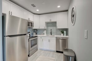A modern kitchen with stainless steel appliances, white cabinetry, and a tiled backsplash.