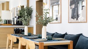 Uma sala de jantar moderna com mesa de madeira posta para quatro pessoas, rodeada por sofás azul escuro.