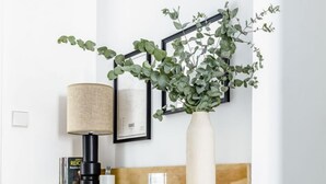 Um interior moderno com um banco de madeira, uma prateleira na parede com objetos decorativos, uma luminária e uma cesta de vime.