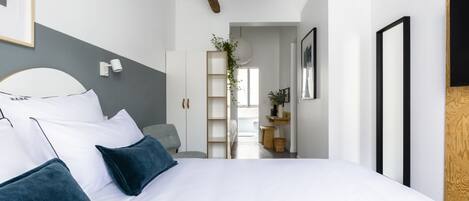 A modern bedroom with a large bed, a grey accent wall, and a wooden ceiling beam.
