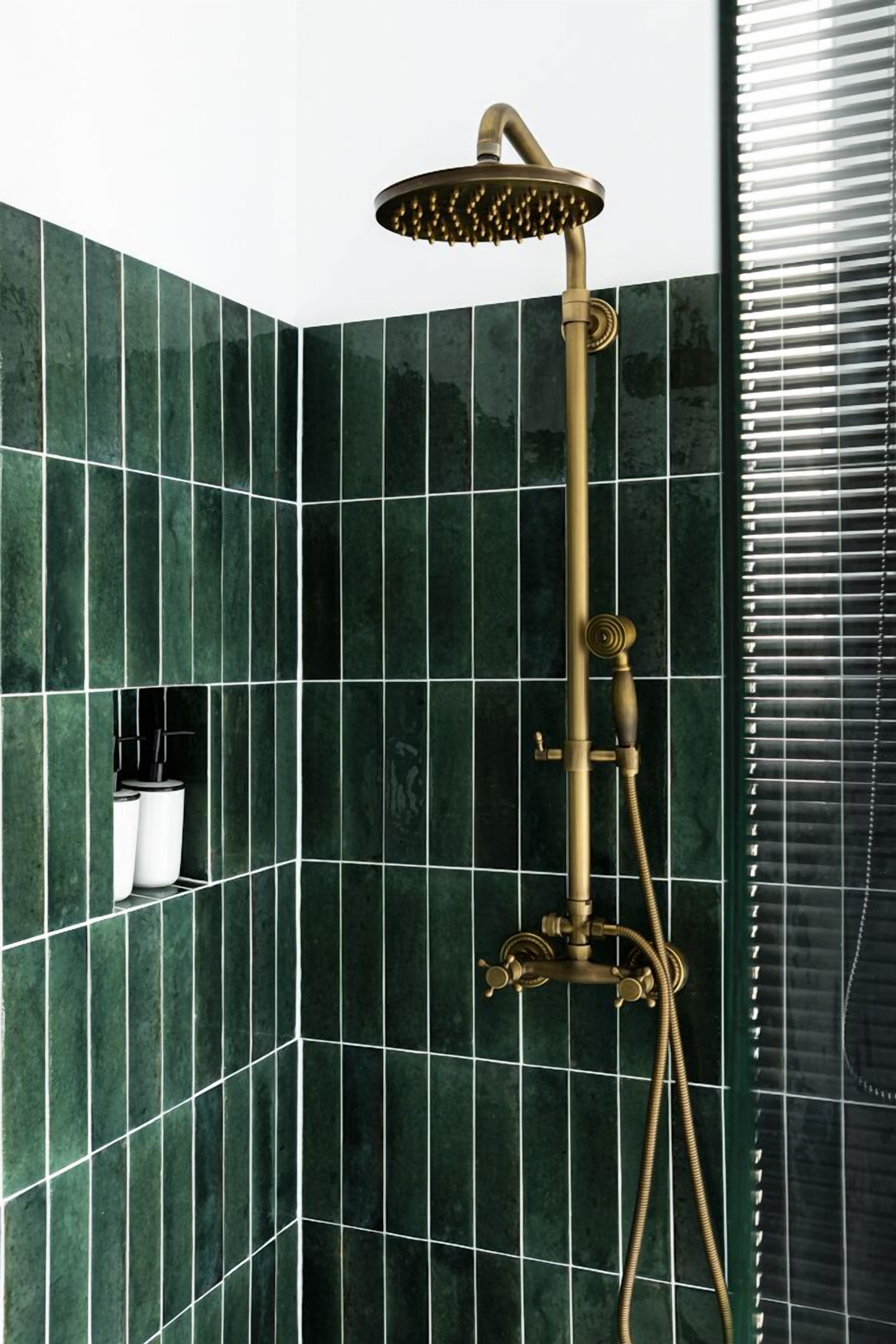 A shower with a gold finish, set against a green tiled wall.
