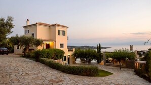 Une maison à deux étages avec une allée pavée de pierres, un petit jardin et une vue sur la mer.