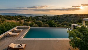 Une piscine à débordement située sur le toit, avec des chaises longues et une vue panoramique sur le paysage.