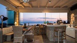 A modern kitchen with a large island, dining area with wicker chairs, and a view of the sea. - Porto Cheli Studio - Poolside Lux Getaway (Porto Cheli)