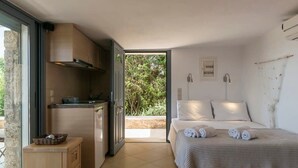 A bedroom with a bed, a small kitchenette, and a sliding glass door leading to a balcony. - Porto Cheli Studio - Poolside Lux Getaway (Porto Cheli)
