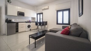 Kompakti oleskelutila, jossa on pieni keittiö, ruokailualue sekä oleskelualue, jossa on sohva ja pöytä.