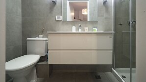 Moderni kylpyhuone, jossa on wc, peilillä varustettu pesuallas ja lasinen suihkuseinä.