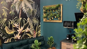 A modern living room with a teal wall, a black and white checkered floor, a green sofa, two wooden side tables, and a ceiling light fixture. - Jungle Apartments II (Wroclaw)