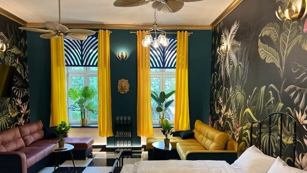 A room with a bed, two sofas, a dining table, and a ceiling fan. - Jungle Apartments II (Wroclaw)