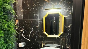 A modern bathroom with black marble tiles, a white sink, and a mirror with a gold frame. - Jungle Apartments II (Wroclaw)