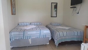 A room with two beds, a television mounted on the wall, and a small table. - pousada estrela matutina (Pirenópolis)
