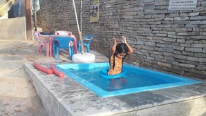 A child playing in a small pool with a stone wall and plastic chairs in the background. - pousada estrela matutina (Pirenópolis)