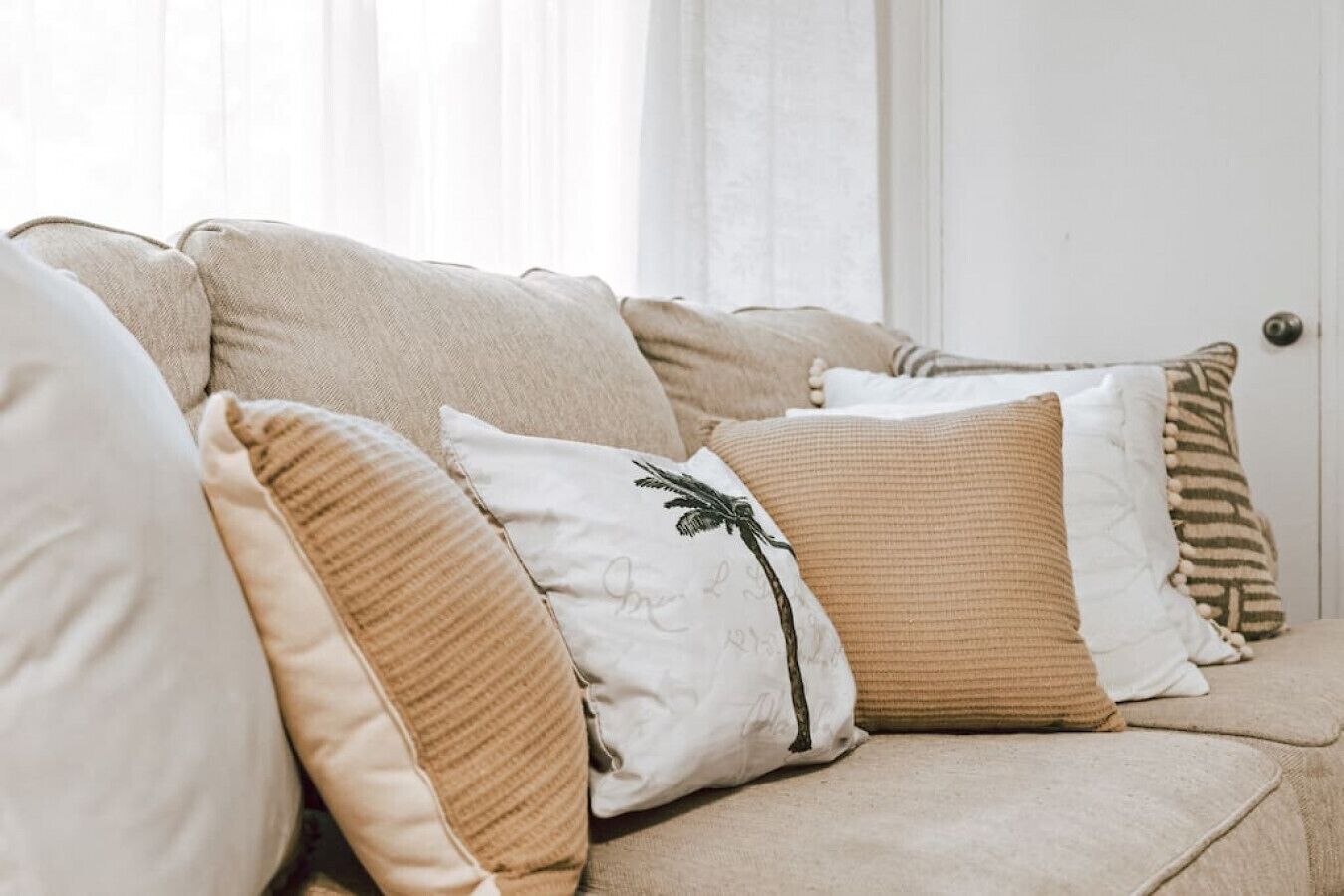 A beige sofa with multiple cushions, including a white one with a black design.
