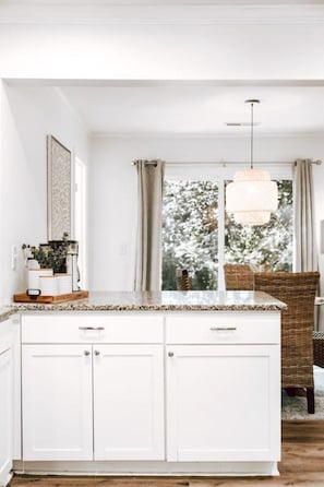 A kitchen with white cabinetry, a wooden countertop, a hanging light fixture, and a view of trees through the window.