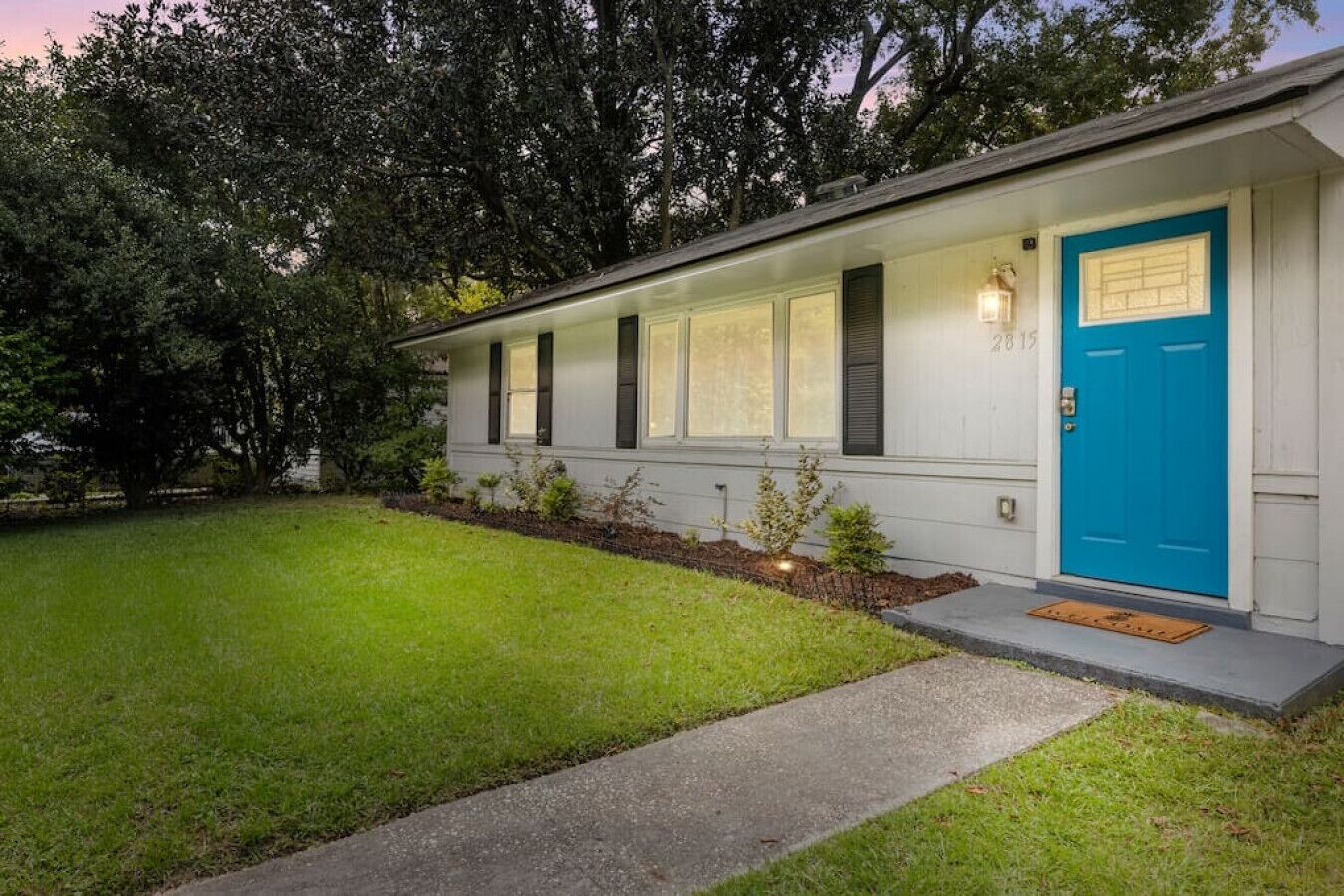 Una casa de un piso con puerta azul, un pequeño porche y un césped cuidado.