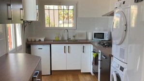 Eine moderne Küche mit Holzboden, weißen Schränken, einer eingebauten Mikrowelle und einer Waschmaschine.