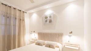 Un dormitorio con cama, mesitas de noche, radiador y una obra de arte colgada en la pared.