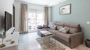 Una sala de estar con un sofá, una mesa de centro, un televisor y una ventana con cortinas.