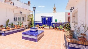 Un patio con suelo de baldosas, plantas en macetas y una pared azul con un diseño decorativo de azulejos.
