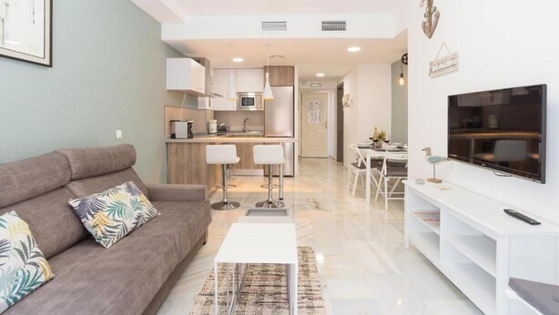 Una sala de estar moderna con un sofá, un televisor y una cocina al fondo.