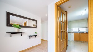 Un corridoio con uno specchio, due mensole a parete con piante e una porta in legno che dà su una cucina con lavastoviglie e una finestra con persiane.